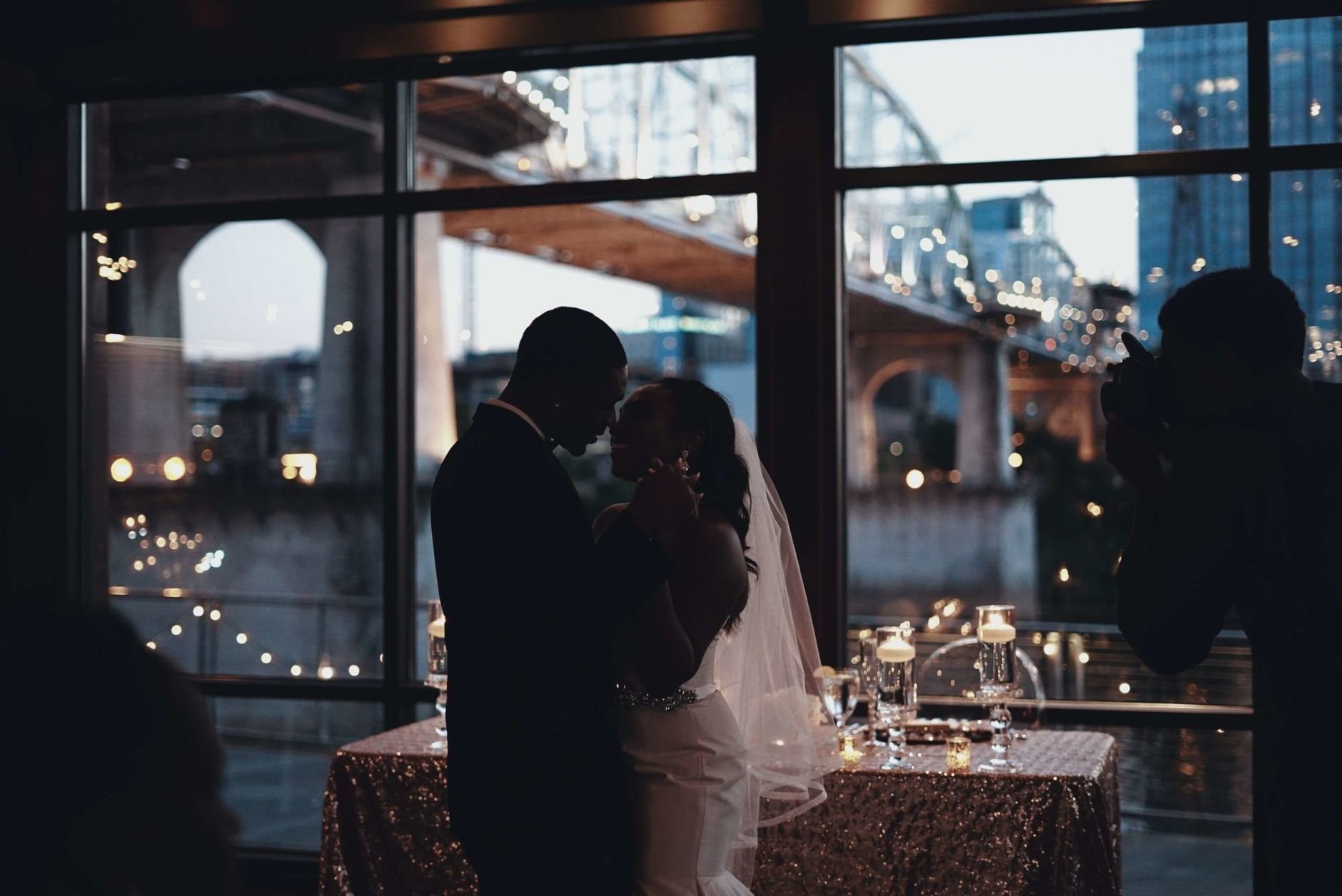 A couple shares a romantic dance at their wedding reception with city lights in the background.
